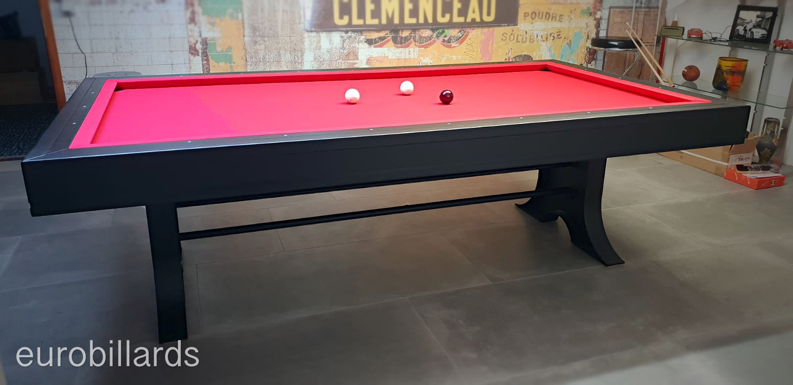 Le système mixte XB breveté par Eurobillards montre clairement sur ce billard ATELIER, les bandes spécifiques aux normes du jeu de billard français qui remplacent celles du jeu américain en respectant la qualité du rebond avec une aisance dans le changement de jeu. Le tissu rouge, reste cohérent sur les deux jeux pour mettre en valeur la finition noire mat du cadre et des gros pied de métal.